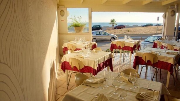 A restaurant with tables set for dining, a view of the beach, and a parked car outside. - Hotel Teti (Ugento)