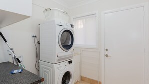 A laundry area with stacked washers and dryers, a mop, and a window with blinds.