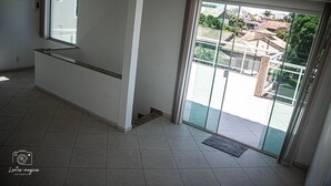 En rummelig stue med en stor skydedør til en balkon, et lille vindue og et flisegulv.