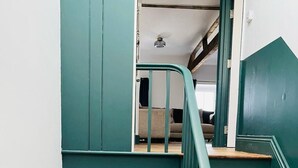 Una escalera con paredes pintadas en color turquesa y peldaños de madera que conduce a un dormitorio con una cama y una mesita de noche.