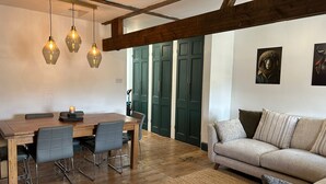 Un comedor con una mesa y sillas de madera, un sofá y una alfombra. Hay tres lámparas colgantes sobre la mesa.
