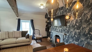 Una sala de estar acogedora con chimenea, una mesa de comedor de madera con una vela y lámparas colgantes.