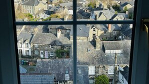 Vista a través de una ventana de un pueblo con edificios de piedra, cielo despejado y colinas a lo lejos.