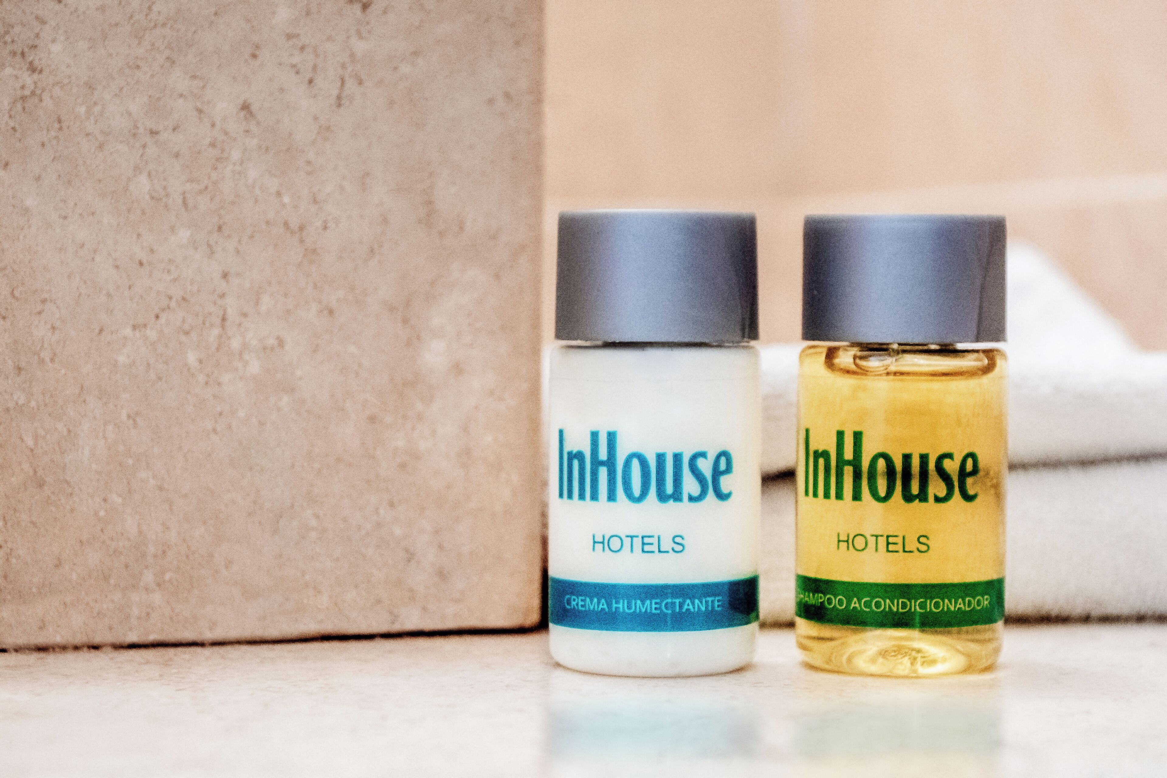 Twee flessen InHouse hotel toiletartikelen, waarvan één 'CREMA HUMECTANTE' en de andere 'SHAMPOO ACONDICIONADOR' is gelabeld.