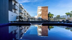 Un hôtel moderne doté d’une piscine dont l’eau reflète le bâtiment et les palmiers.