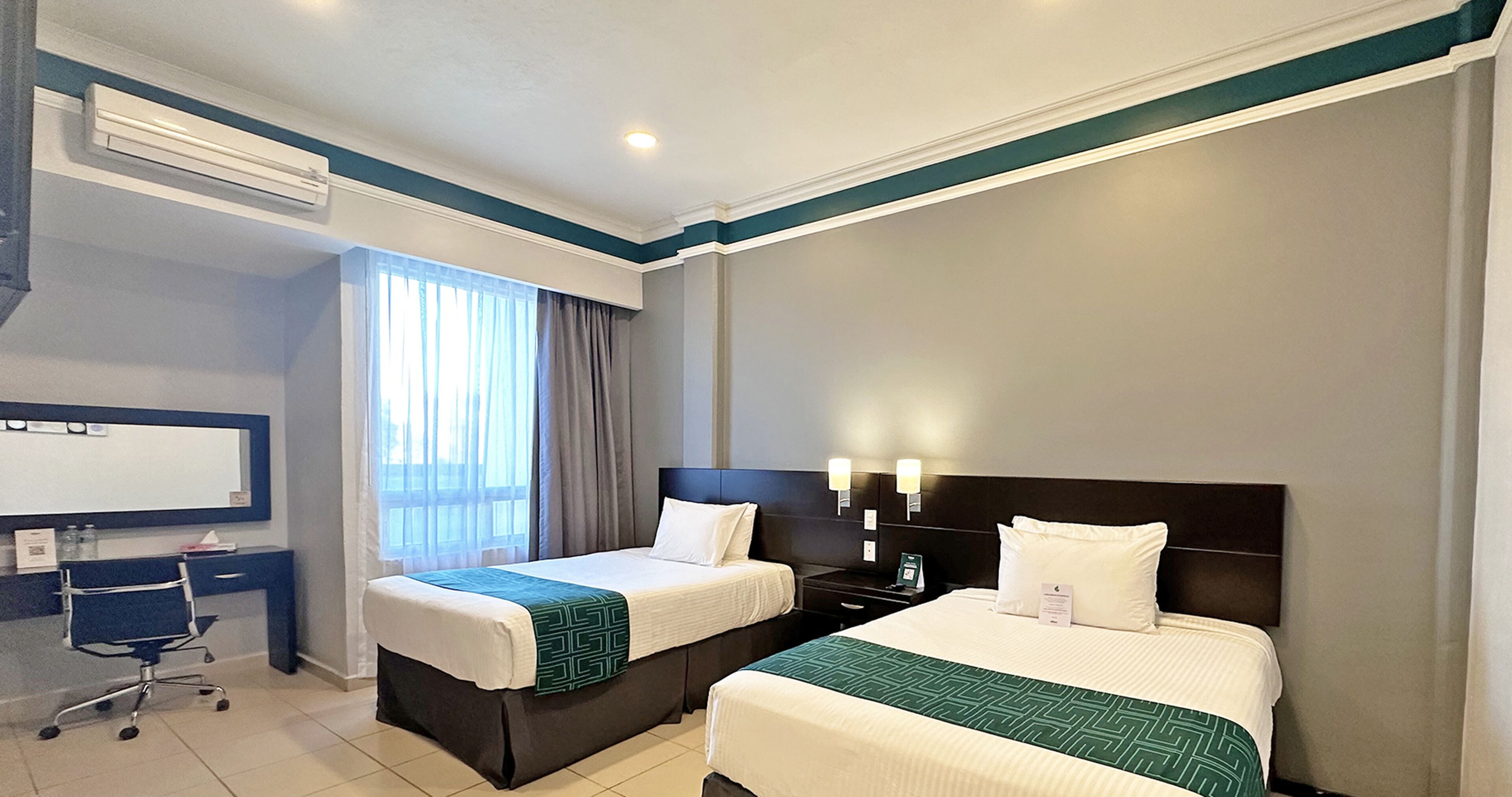 Habitación de hotel con dos camas, un escritorio, una silla, un televisor y una ventana con cortinas.