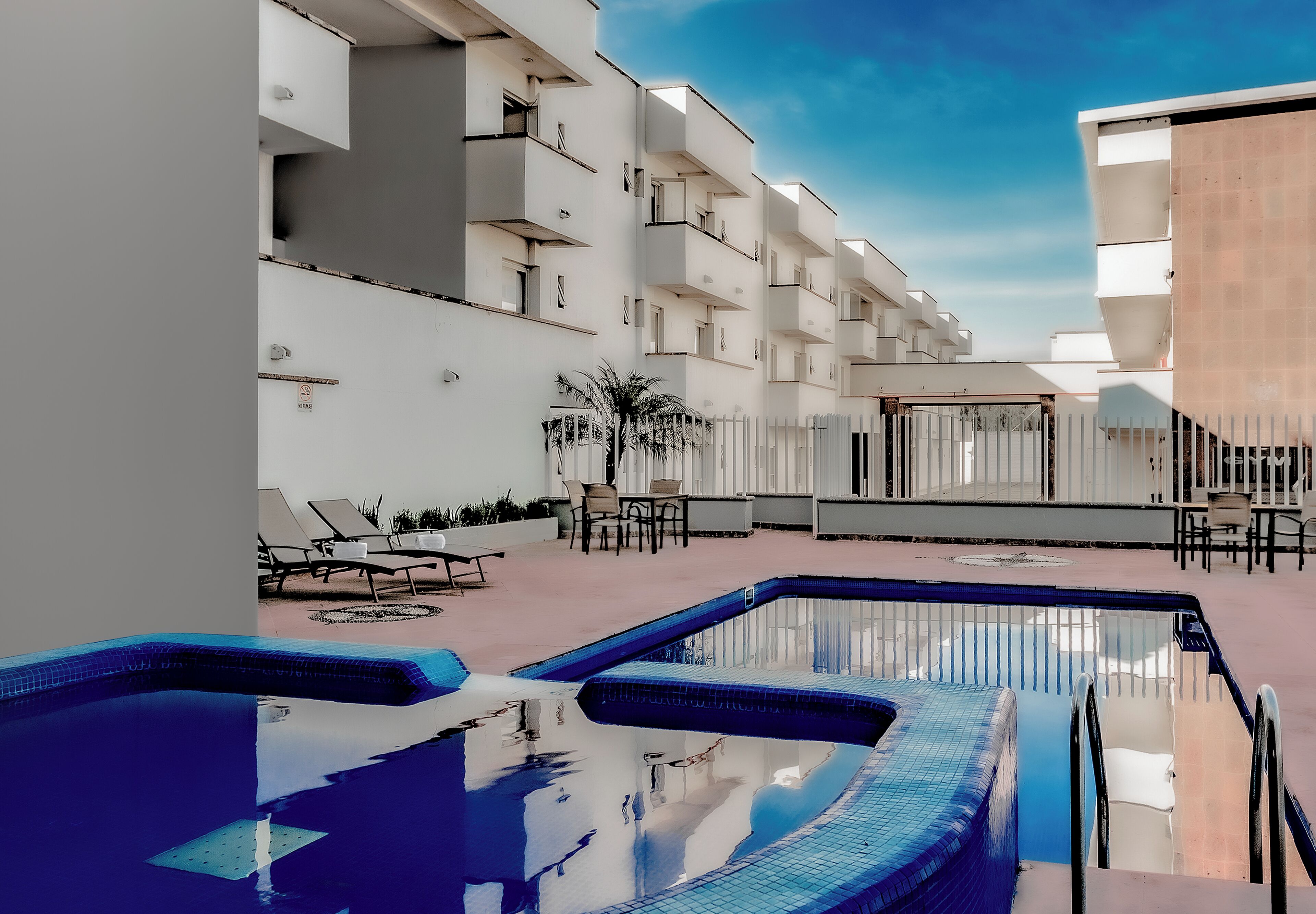 A modern hotel with a rooftop pool, white balconies, and outdoor seating areas.