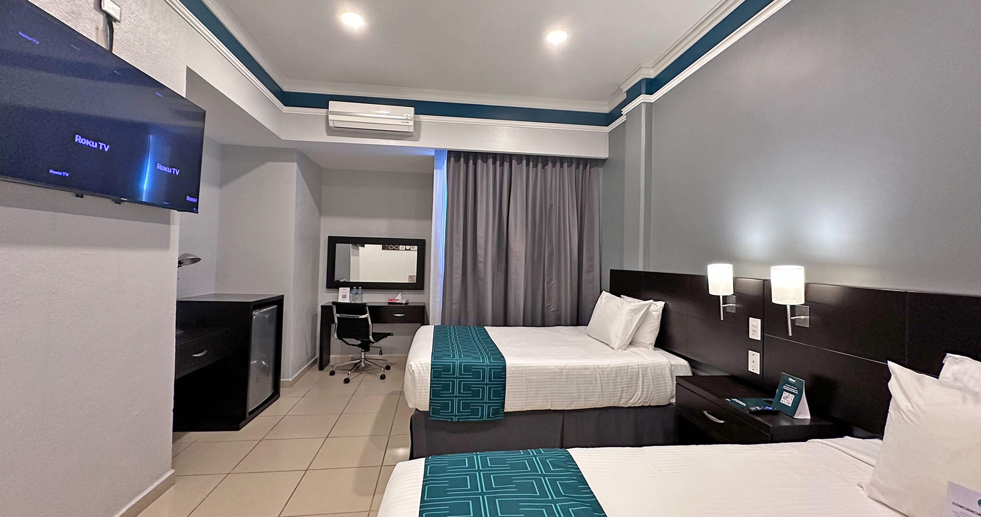 A hotel room with two beds, a desk, a TV, and a mirror.