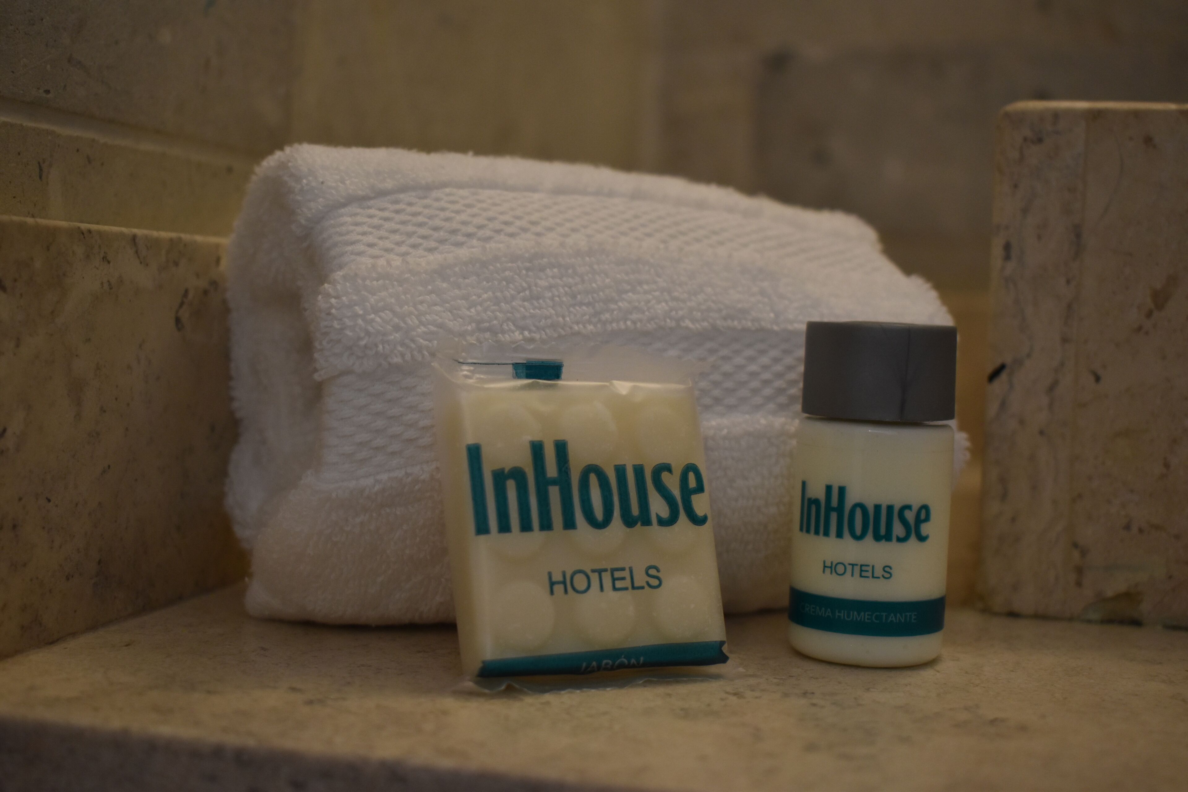 A bathroom with a white towel and two InHouse Hotels toiletries.