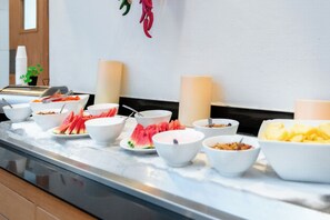 A buffet setup with various food items and bowls on a marble countertop.