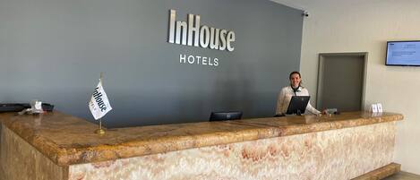 Un mostrador de recepción en InHouse Hotels, con encimera de mármol, una bandera y una pantalla digital mostrando información.