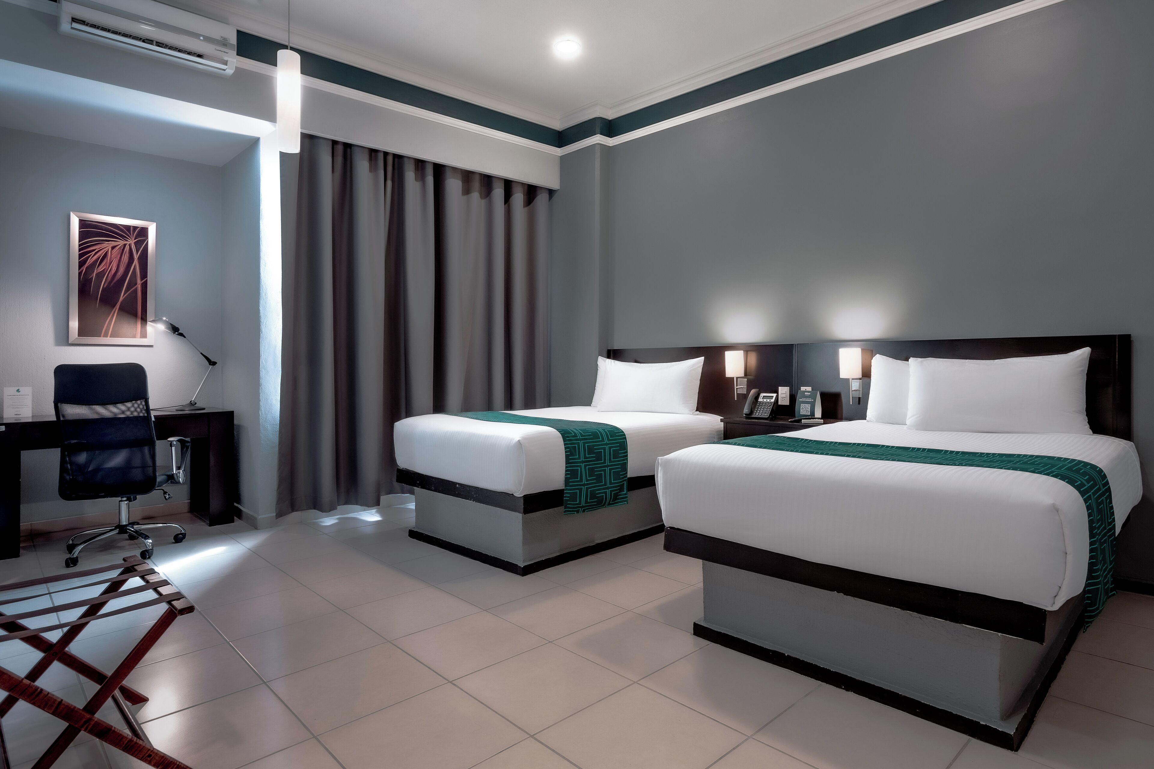A hotel room with two beds, a desk, a chair, and a large window with curtains.