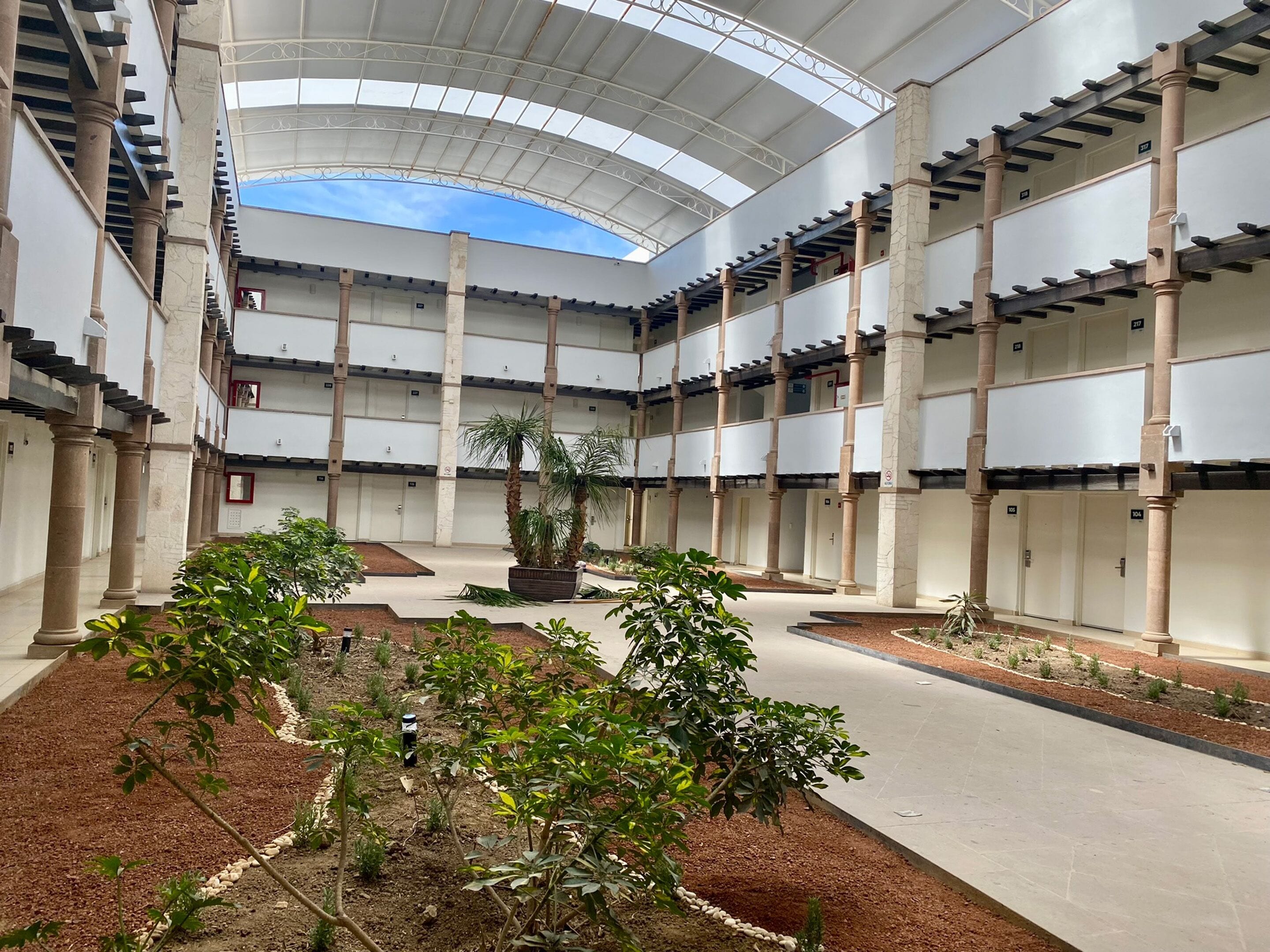 Un vaste atrium doté d’un haut plafond et baigné de lumière naturelle, avec un jardin central agrémenté de plantes et d’un banc où s’asseoir.
