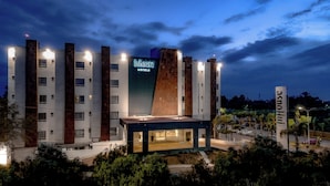 Un hôtel moderne, reconnaissable à son panneau « InHouse Hotels » bien visible, qui se distingue par son architecture originale, caractérisée par un mélange de façades blanches et brunes.