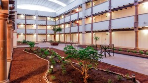 Un atrium à plusieurs niveaux doté d’un jardin central, de nombreux espaces de détente et d’un design architectural moderne avec des colonnes apparentes et un plafond en verre.