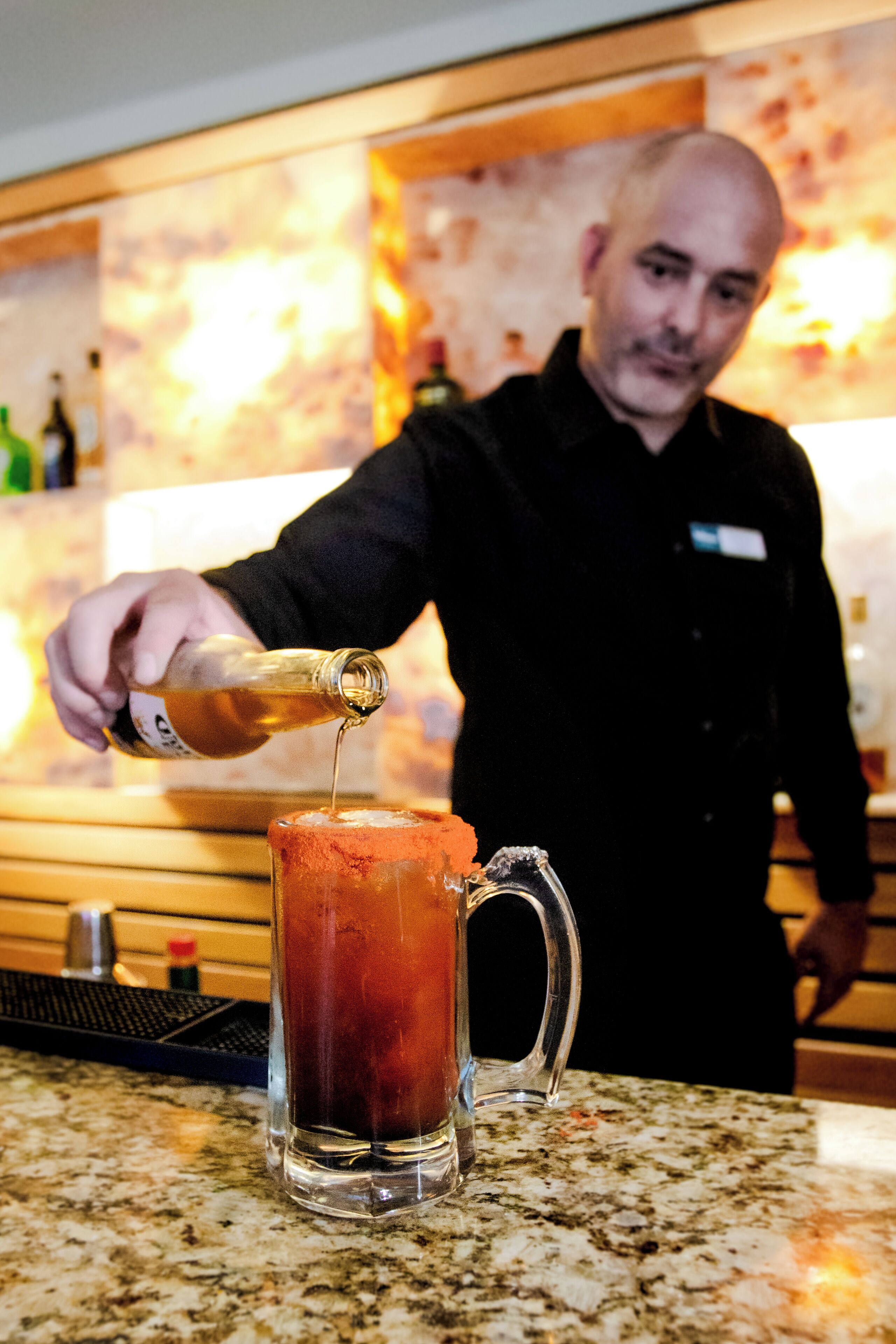 Un barman abocant una beguda en un got de vidre transparent sobre una superfície de pedra granítica.