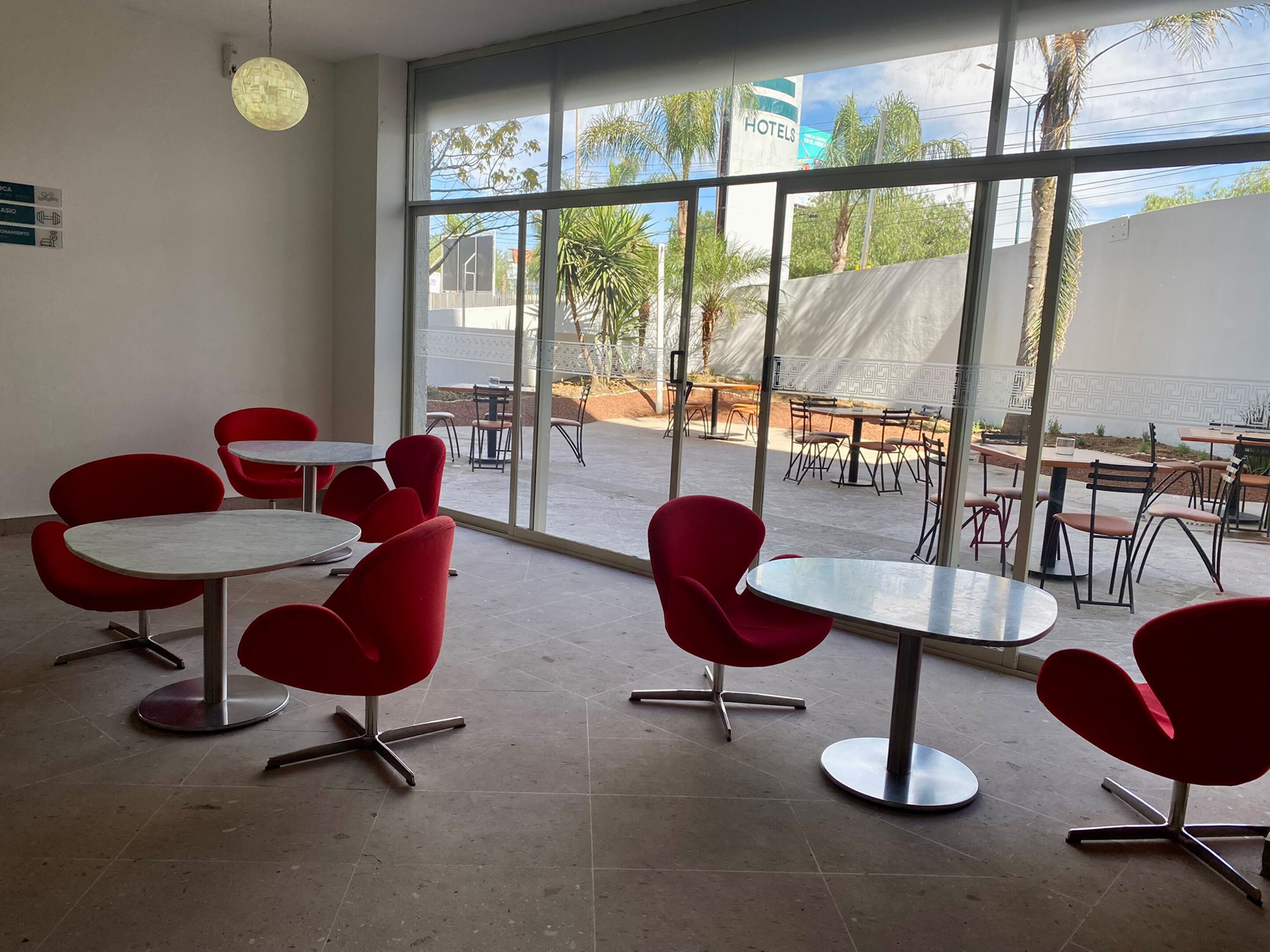 A modern indoor seating area with red chairs and tables, large windows offering a view of the outdoor patio area.