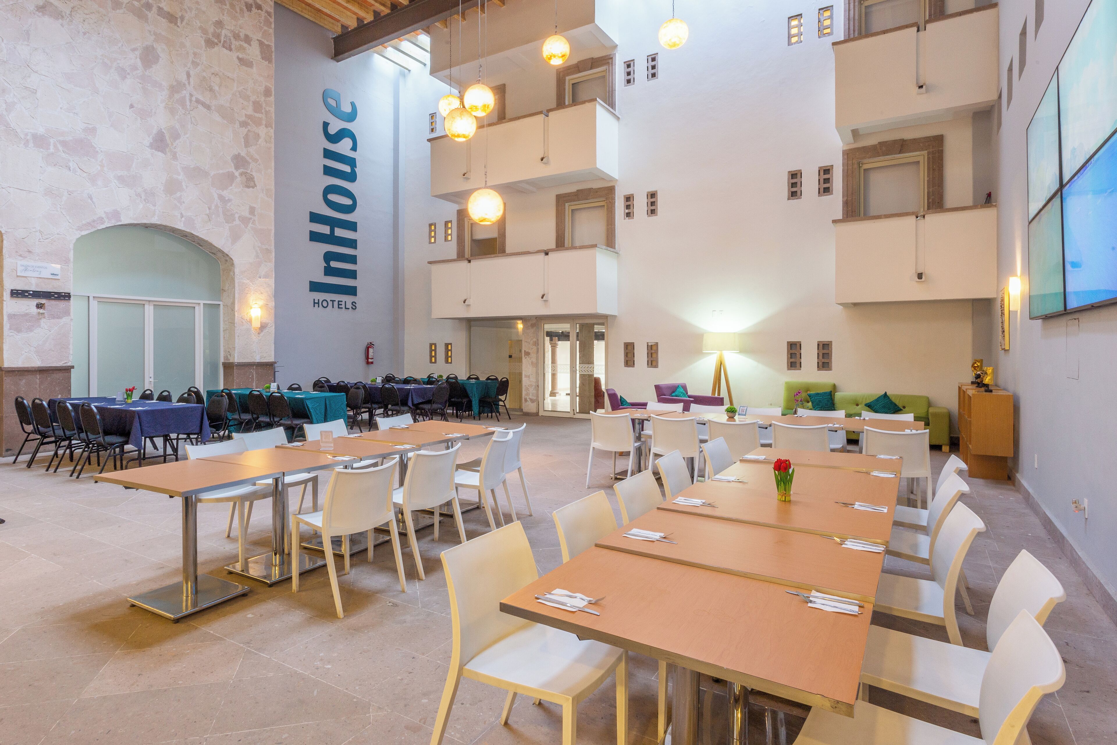 Un comedor de hotel con varias mesas y sillas, una pared de piedra y un letrero que dice "InHouse Hotels".