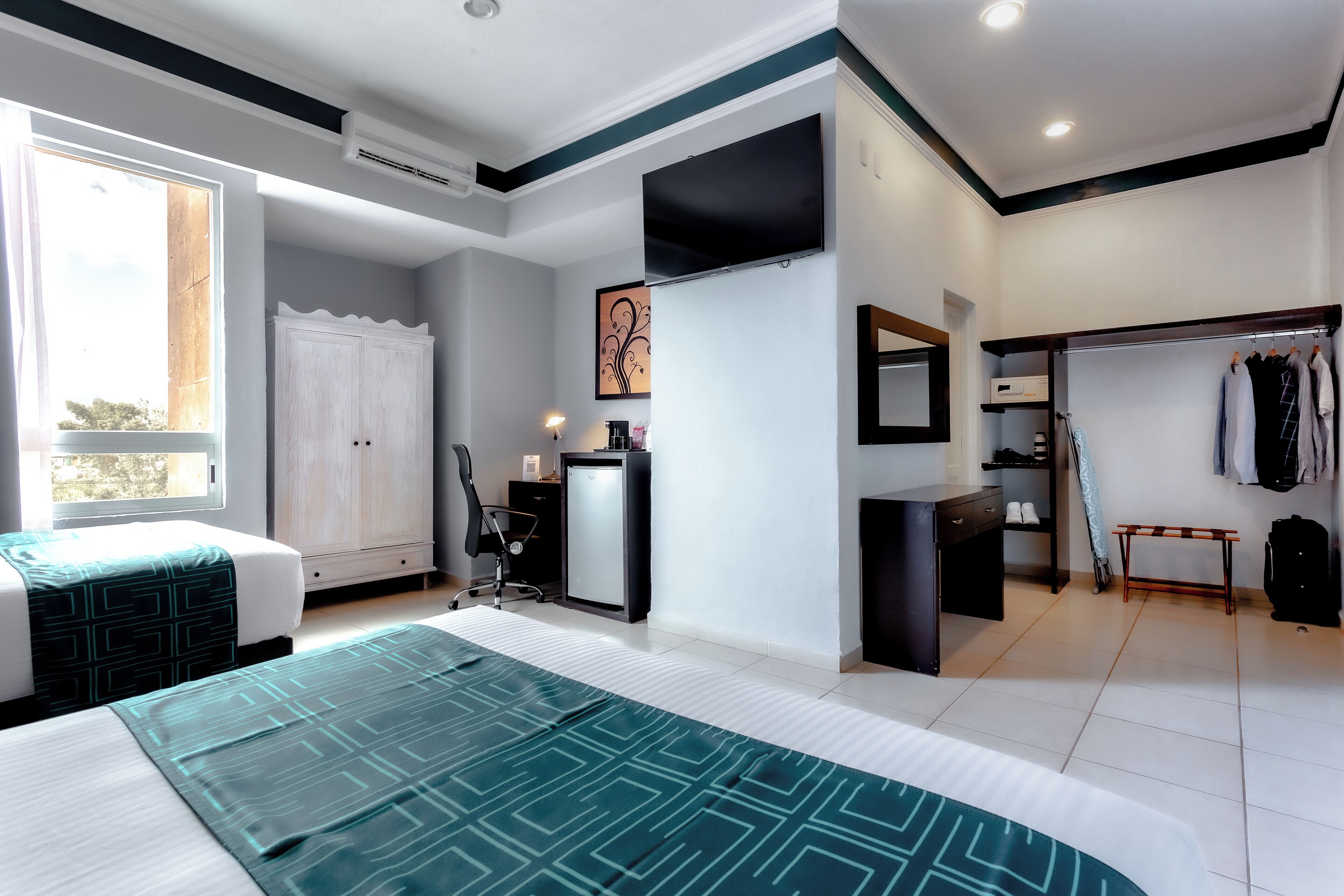 Habitación de hotel moderna con una cama grande, un escritorio, una silla, un armario y un vestidor con ropa colgada.