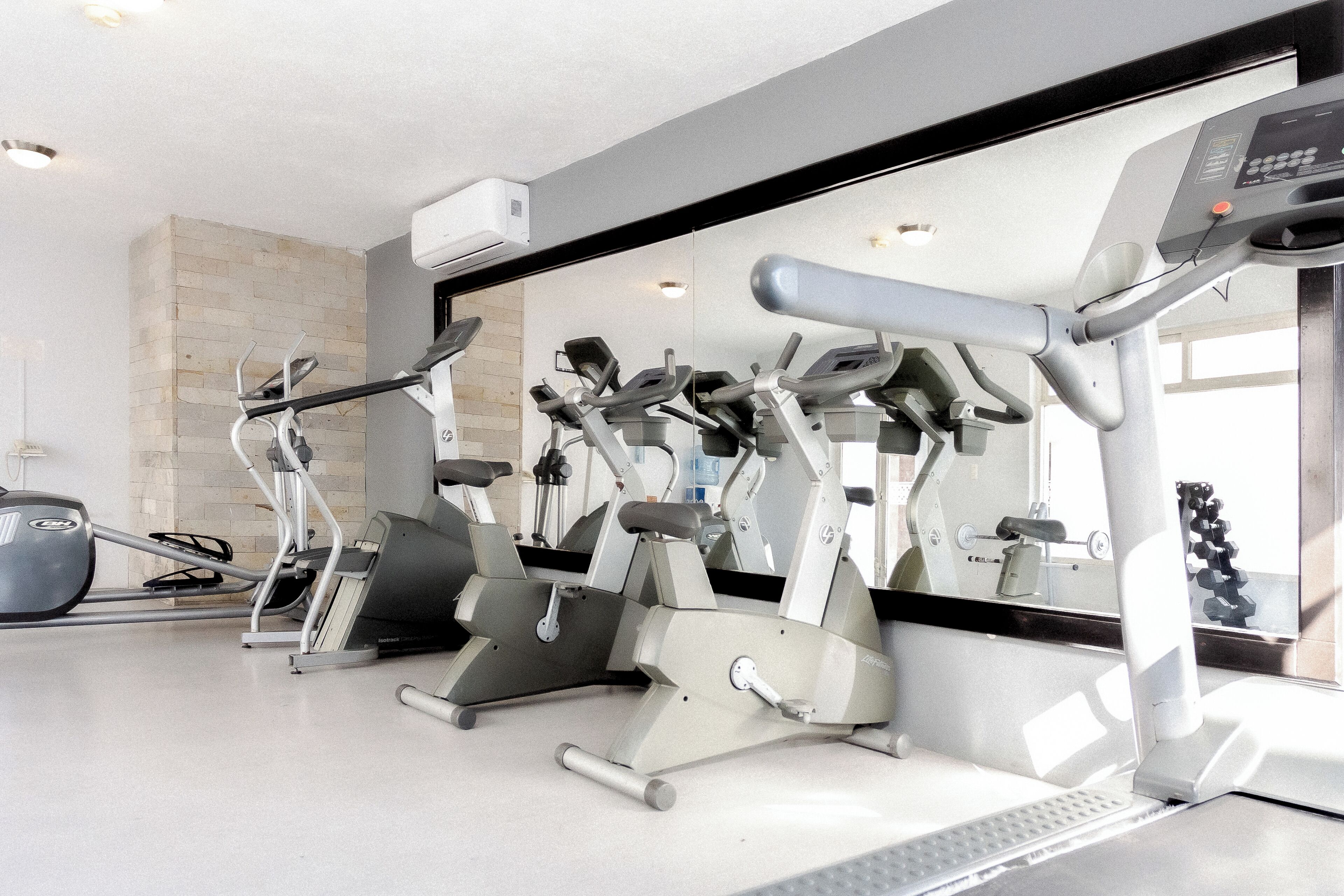 A gym with various exercise machines, a large mirror, and a window with natural light.