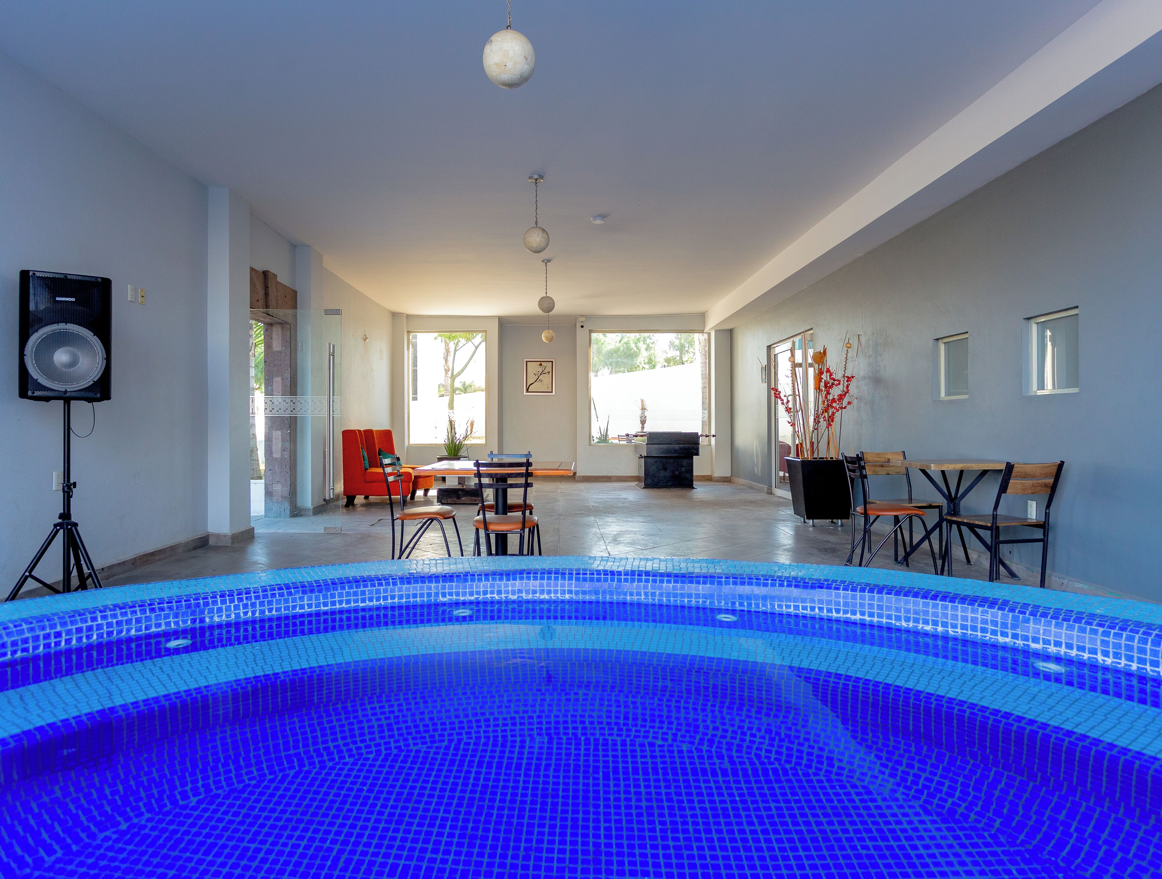 An indoor swimming pool with a tiled floor, a seating area with chairs and a table, and a speaker on a tripod.
