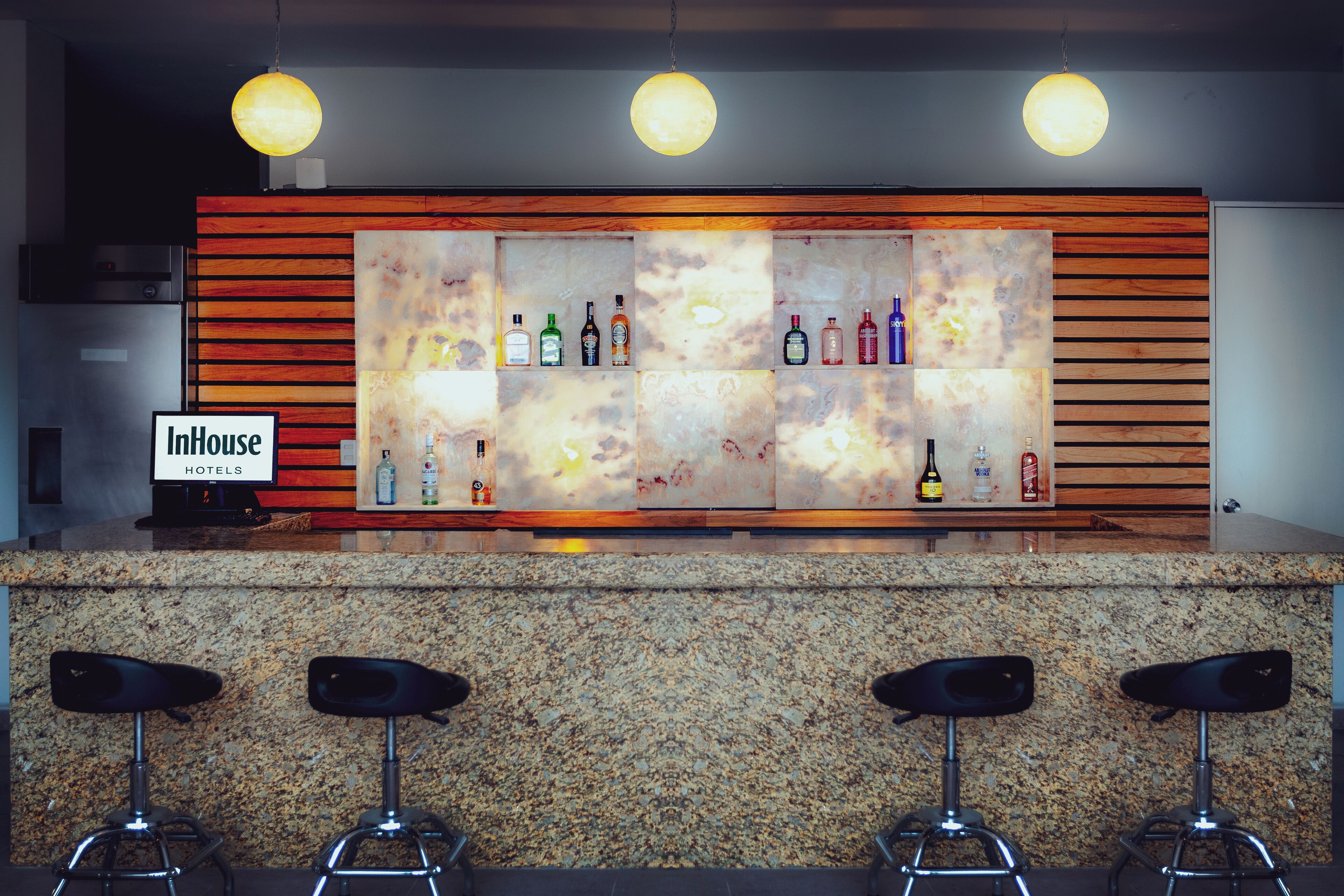 A bar area with a wooden panel wall, a variety of liquor bottles, and three bar stools.
