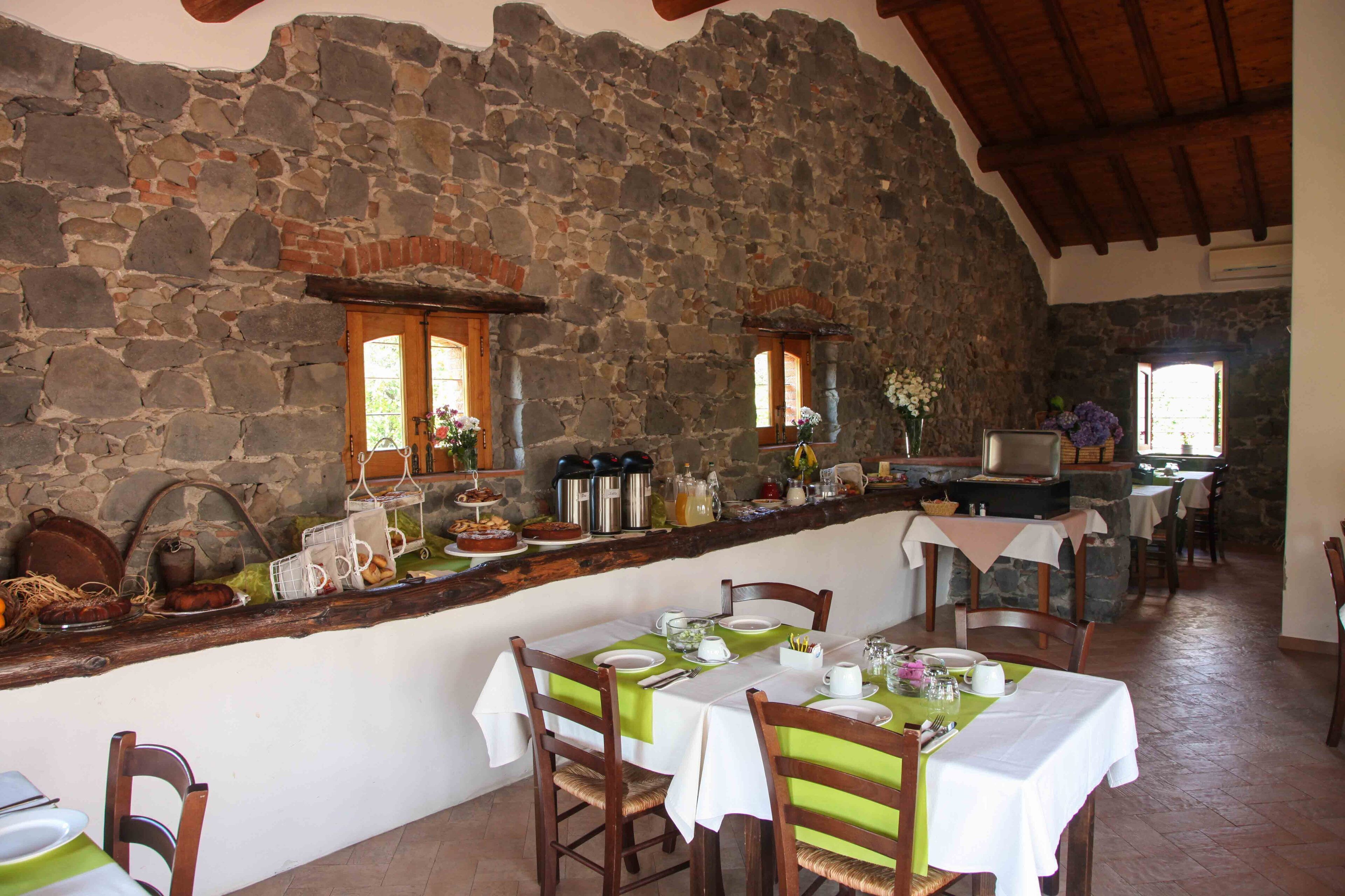 Un'area pranzo rustica con pareti in pietra, travi in legno, un bancone in pietra con stoviglie e un tavolo apparecchiato per quattro.