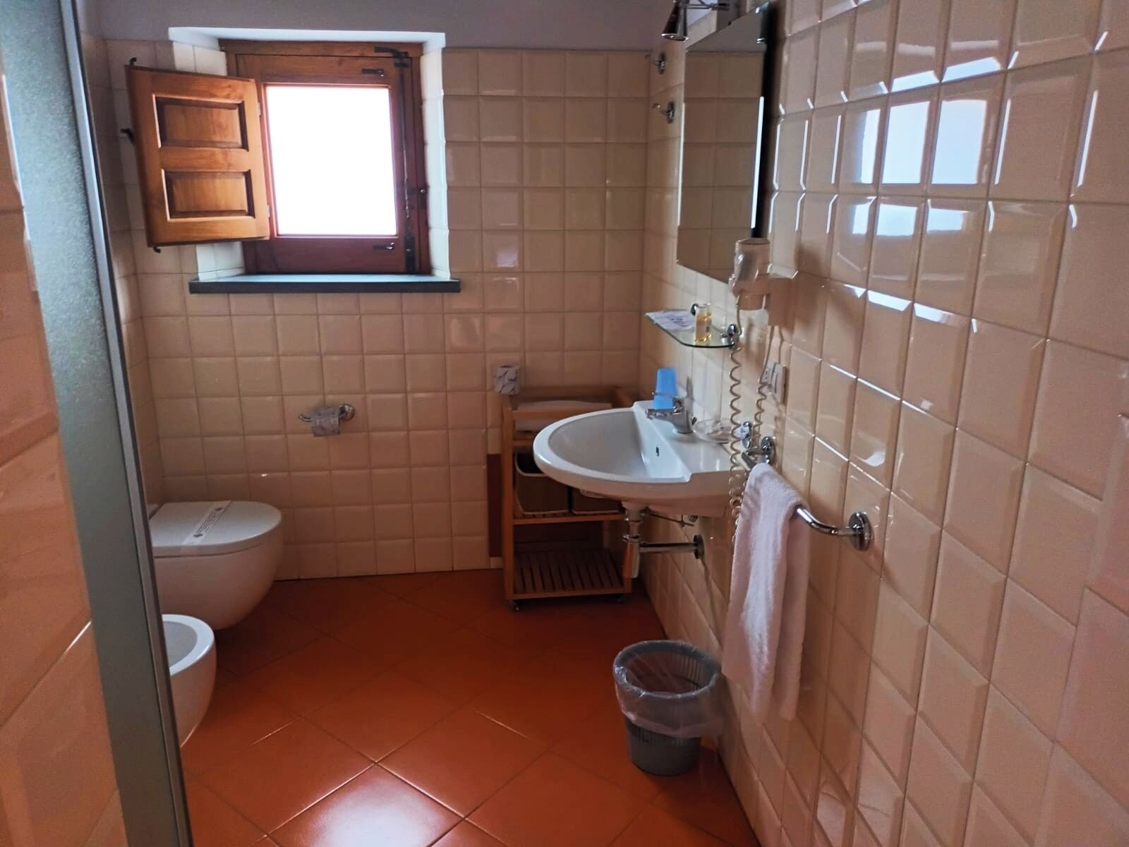 Un baño pequeño con inodoro, lavamanos y una ventana sobre el inodoro.