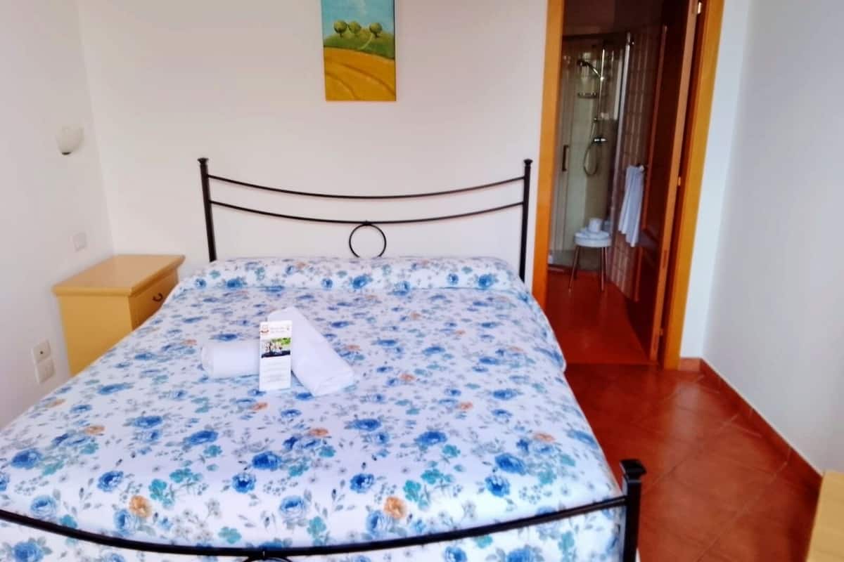 A bed with a floral bedspread, a wooden nightstand, and a painting on the wall.