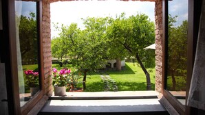 A view through a window with a brick frame, leading to a grassy yard with trees and potted plants. - Agriturismo Galea (Riposto)