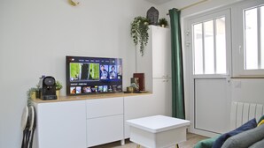 Una sala de estar moderna con un televisor de pantalla plana montado sobre un mueble blanco, una mesita pequeña blanca y una cortina verde.