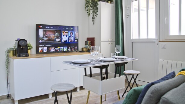 Una cocina moderna con comedor, un televisor montado en la pared y un ventanal con cortinas.