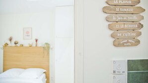 Un dormitorio con cabecera de madera, una mesita de noche con lámpara y un letrero en la pared con frases en francés.