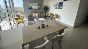 Ein modernes Wohnzimmer mit einem grauen Sofa, gelben Sesseln, einem Couchtisch und einem Essbereich mit weißen Stühlen.