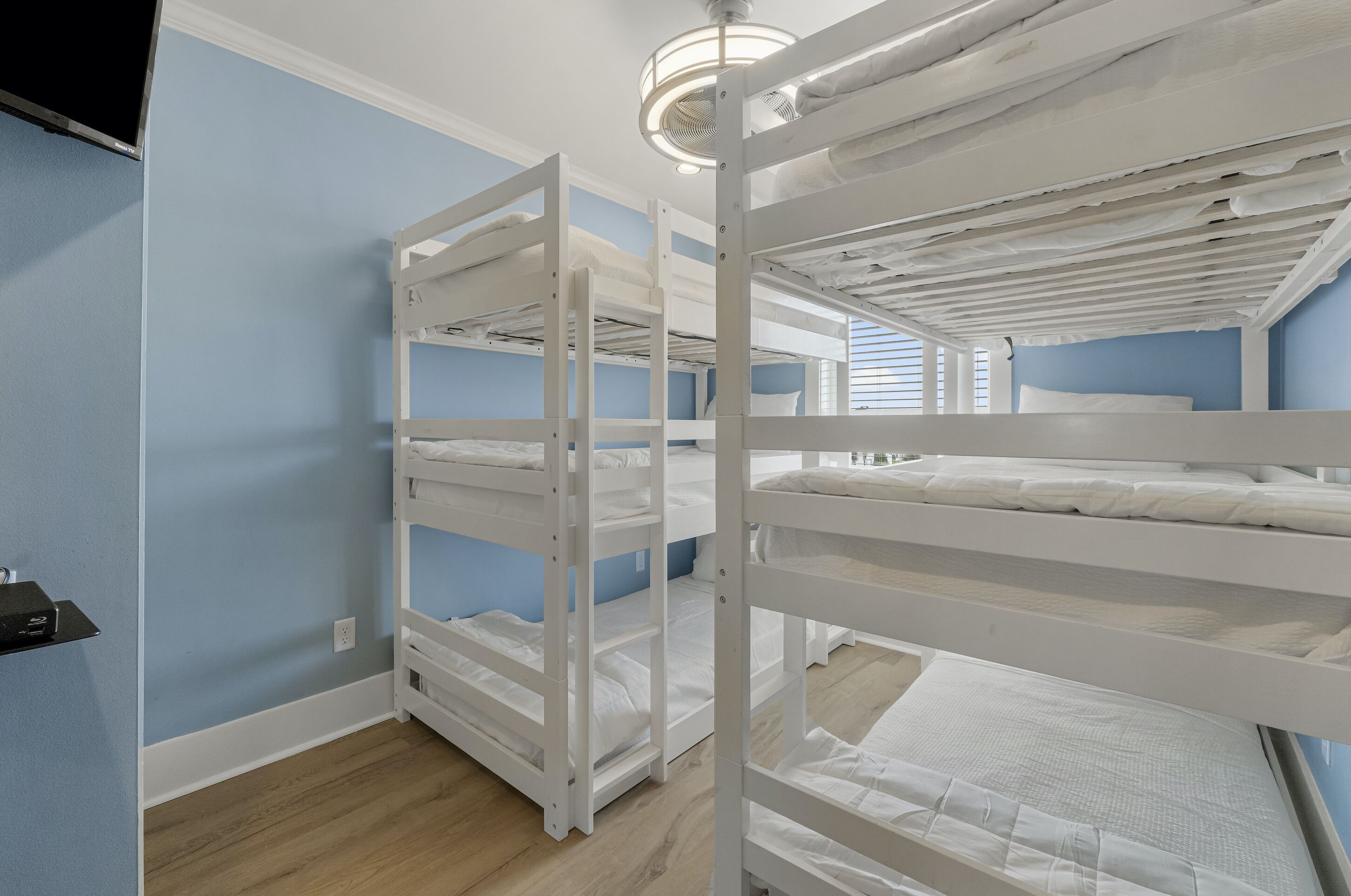 A room with bunk beds, a ceiling fan, and a TV mounted on the wall.