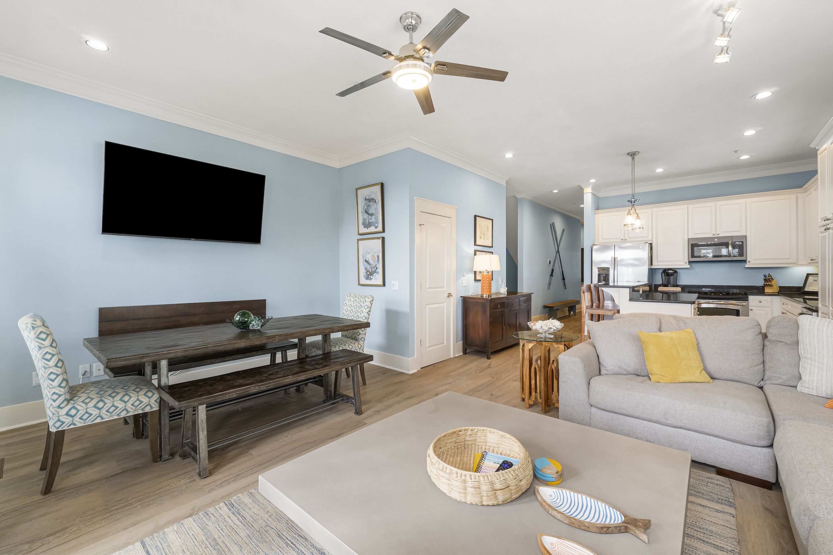 A modern living room with a dining area, a kitchen, and a ceiling fan.