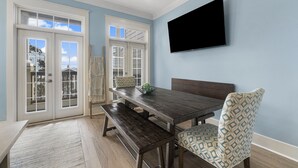 Ein Essbereich mit Holztisch, Bank, gemusterten Stühlen und einem an der Wand befestigten Fernseher.