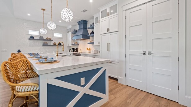 A modern kitchen with white cabinets, a blue accent wall, and a dining area with wicker chairs. - Rooftop Deck, Private Pool and Game room! Perfect for Families! (Anna Maria)
