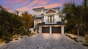 A two-story house with a driveway leading to a garage, surrounded by palm trees and a landscaped garden. - Rooftop Deck, Private Pool and Game room! Perfect for Families! (Anna Maria)