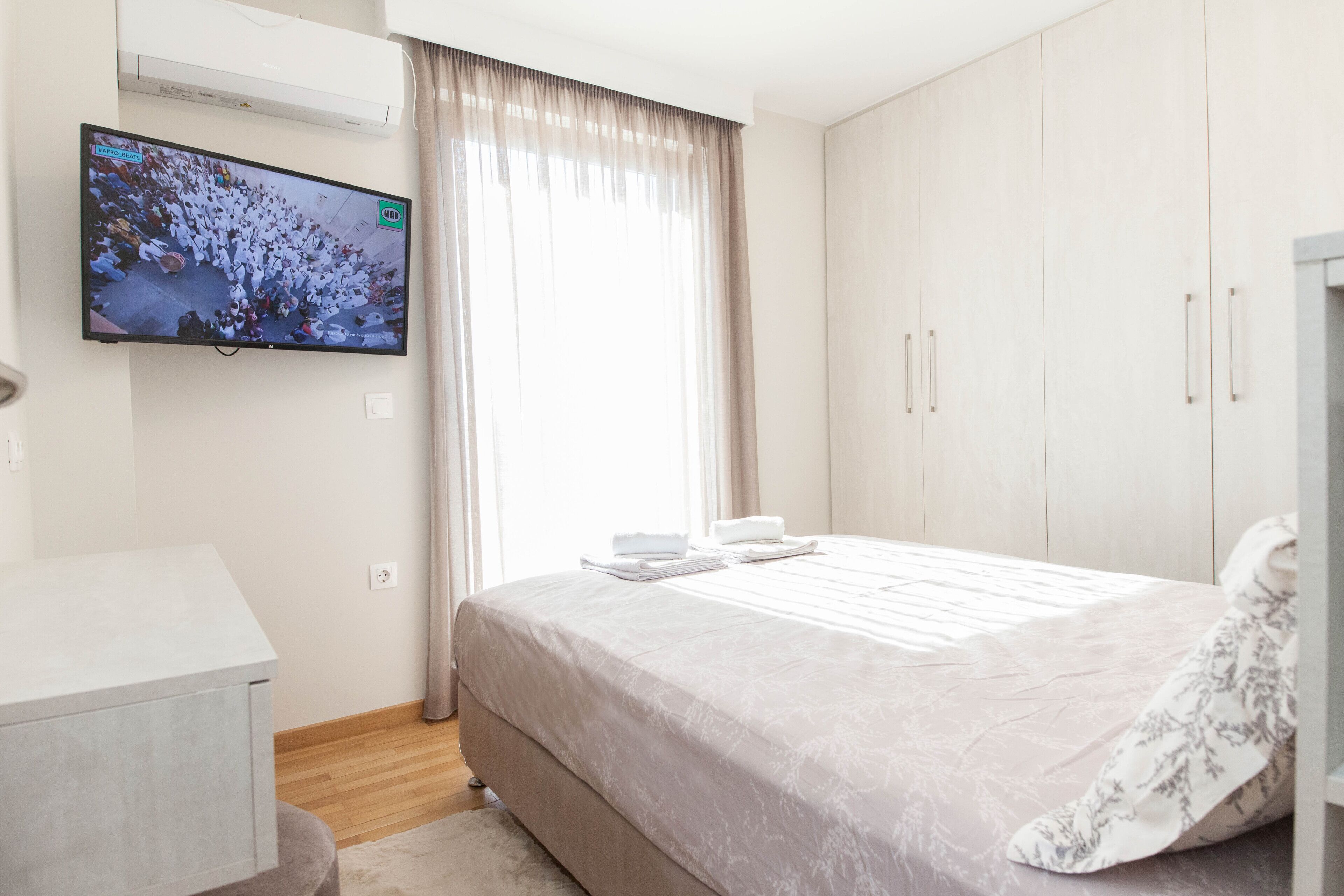 Une chambre d’hôtel avec un lit, un téléviseur fixé au mur, une armoire et une fenêtre avec des rideaux.