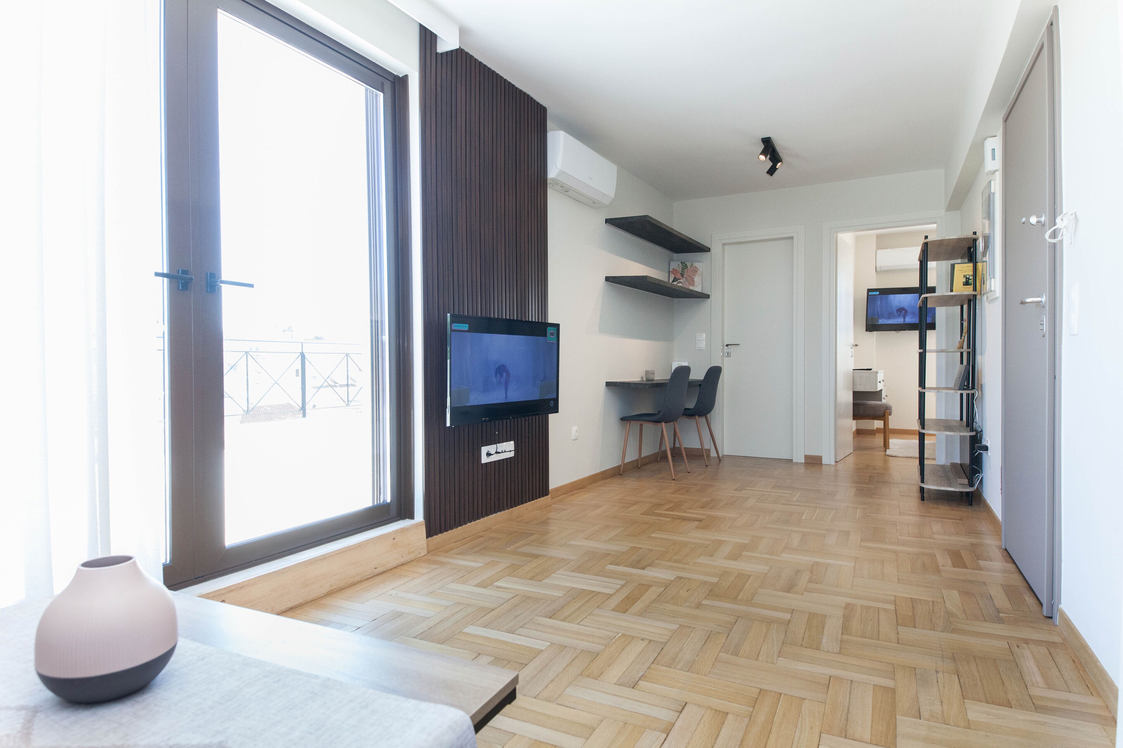 A modern living room with a large TV, wooden flooring, and a dining area with chairs.