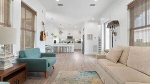 A modern living room with a sofa, a coffee table, and a rug. There is a kitchen in the background with a dining area. - Experience Seajoy! 200 yard walk to beach! (Orange Beach)