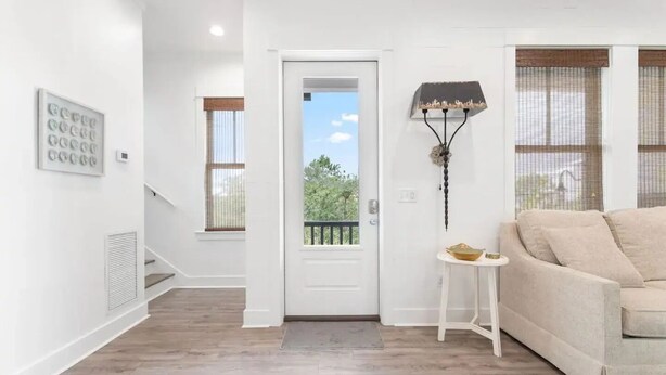 A modern living room with a beige sofa, a small white side table, a decorative floor lamp, and a door leading to a balcony. - Experience Seajoy! 200 yard walk to beach! (Orange Beach)