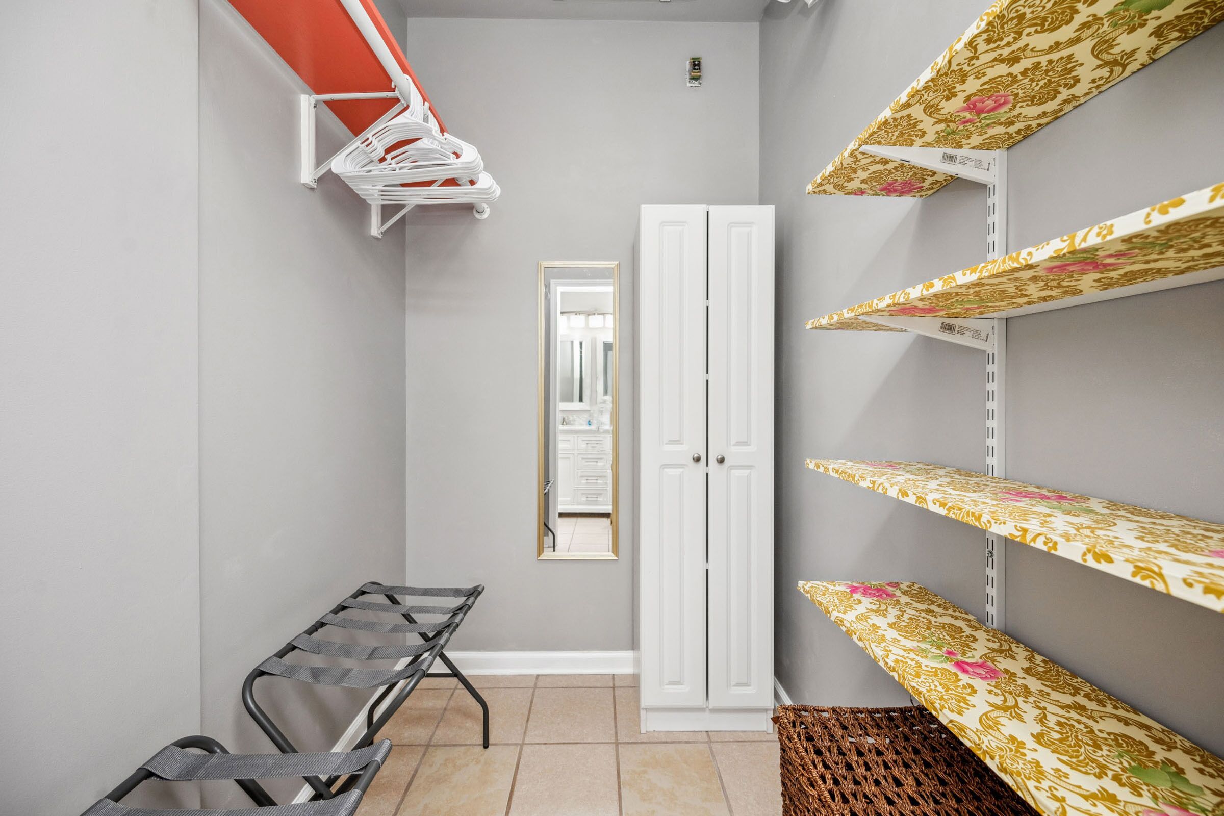 A narrow hallway with a metal bench, a white wardrobe, and shelves with patterned fabric.