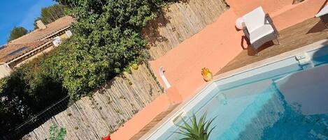 A swimming pool with a wooden deck, surrounded by a fence and potted plants.