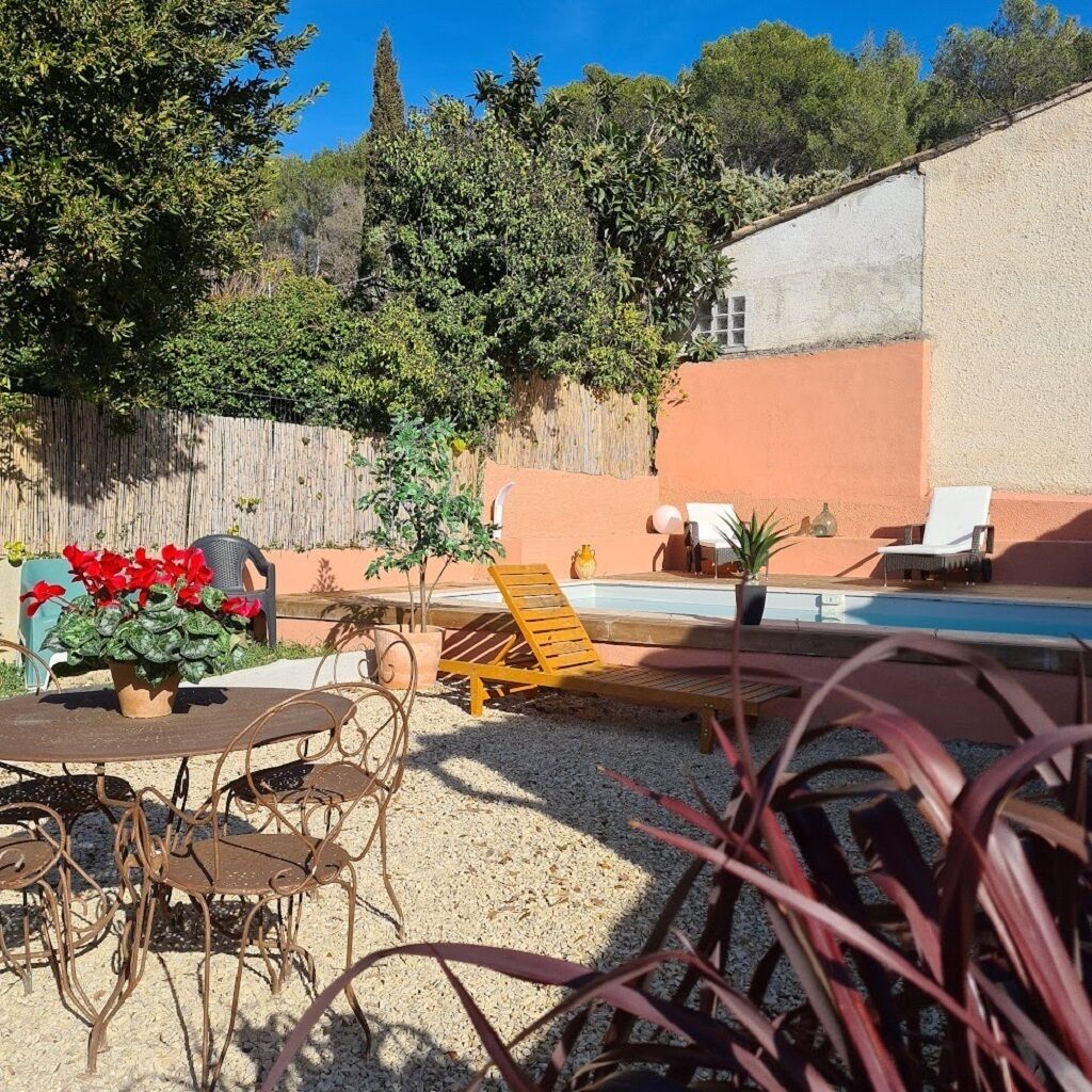 Un espace piscine aménagé avec une table et des chaises, entouré de verdure et délimité par une clôture en bois.