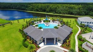 A resort with a central swimming pool, surrounded by manicured lawns and palm trees, with a lake in the background.