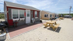 Een gebouw aan het strand met een terras, picknicktafels en een barbecue.