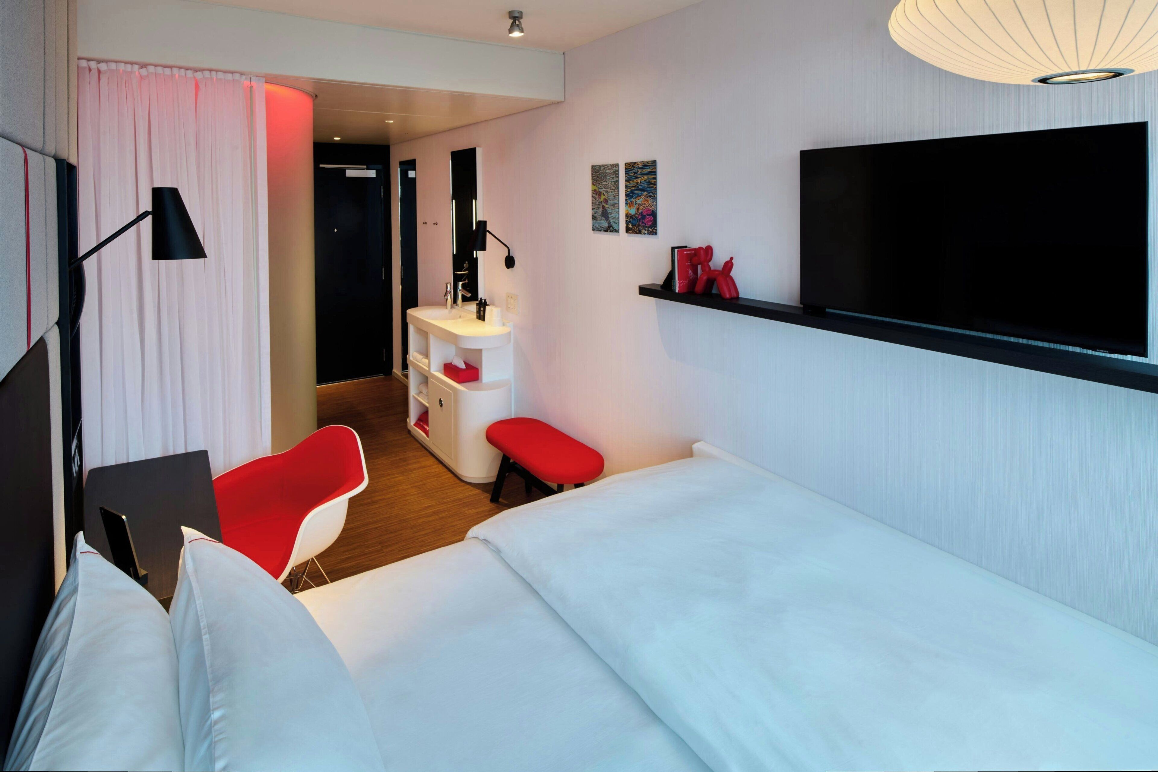 Habitación de hotel con cama, escritorio, silla, tocador con espejo, televisor y una obra de arte en la pared.