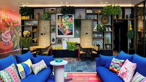 A modern living room with blue sofas, a coffee table, and a colorful rug. There are shelves with decorative items and a large painting on the wall. - citizenM Miami South Beach (Miami Beach)